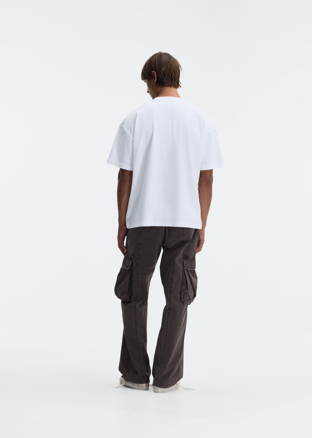 A model shown from the back wearing a white oversized short-sleeve t-shirt and dark brown wide-leg cargo pants, standing against a seamless white studio background.