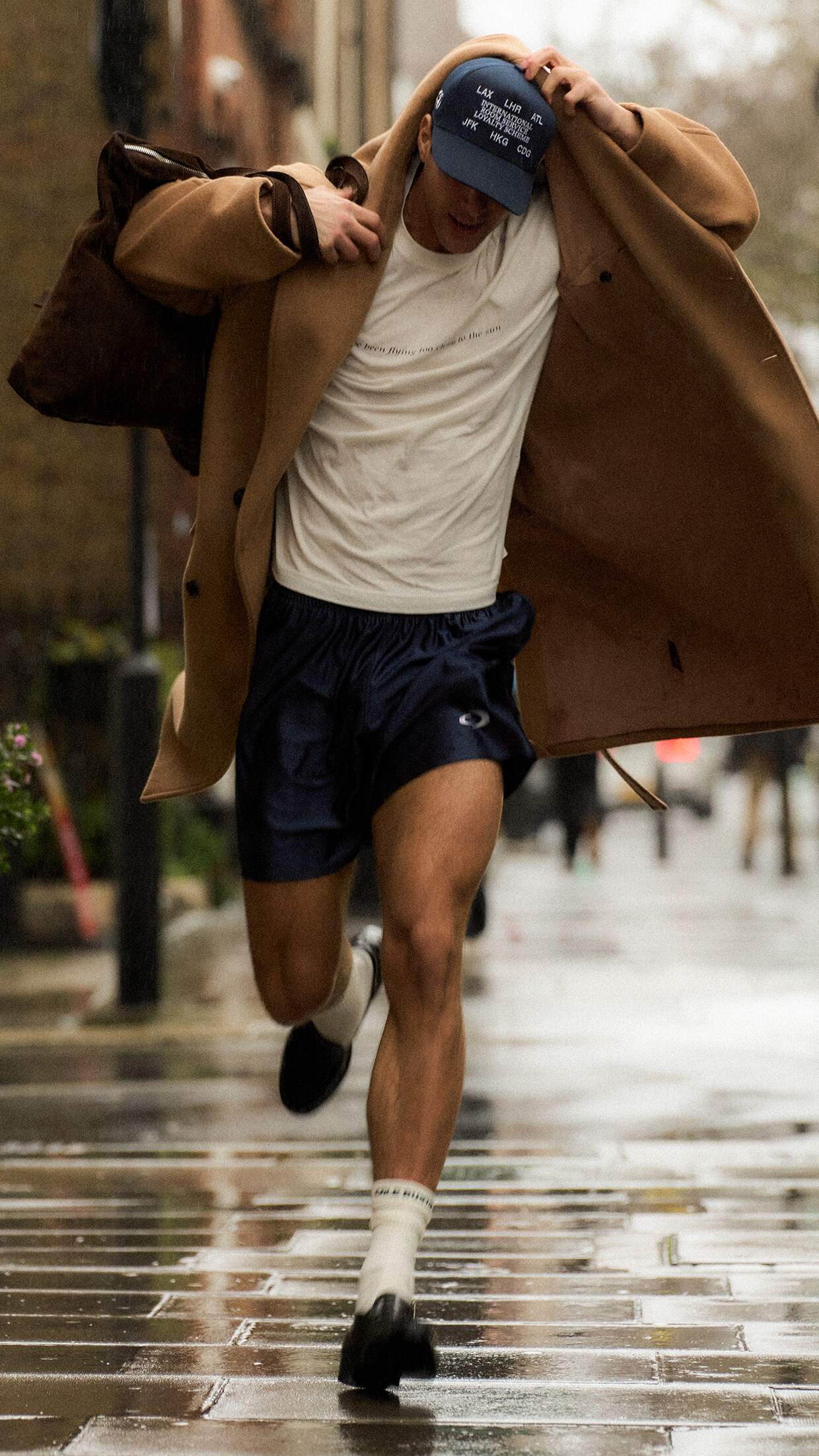 Person wearing a tan coat lying on a couch with a checkered rug in the background